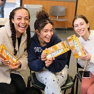 3 students smile while holding a pack of thermometers